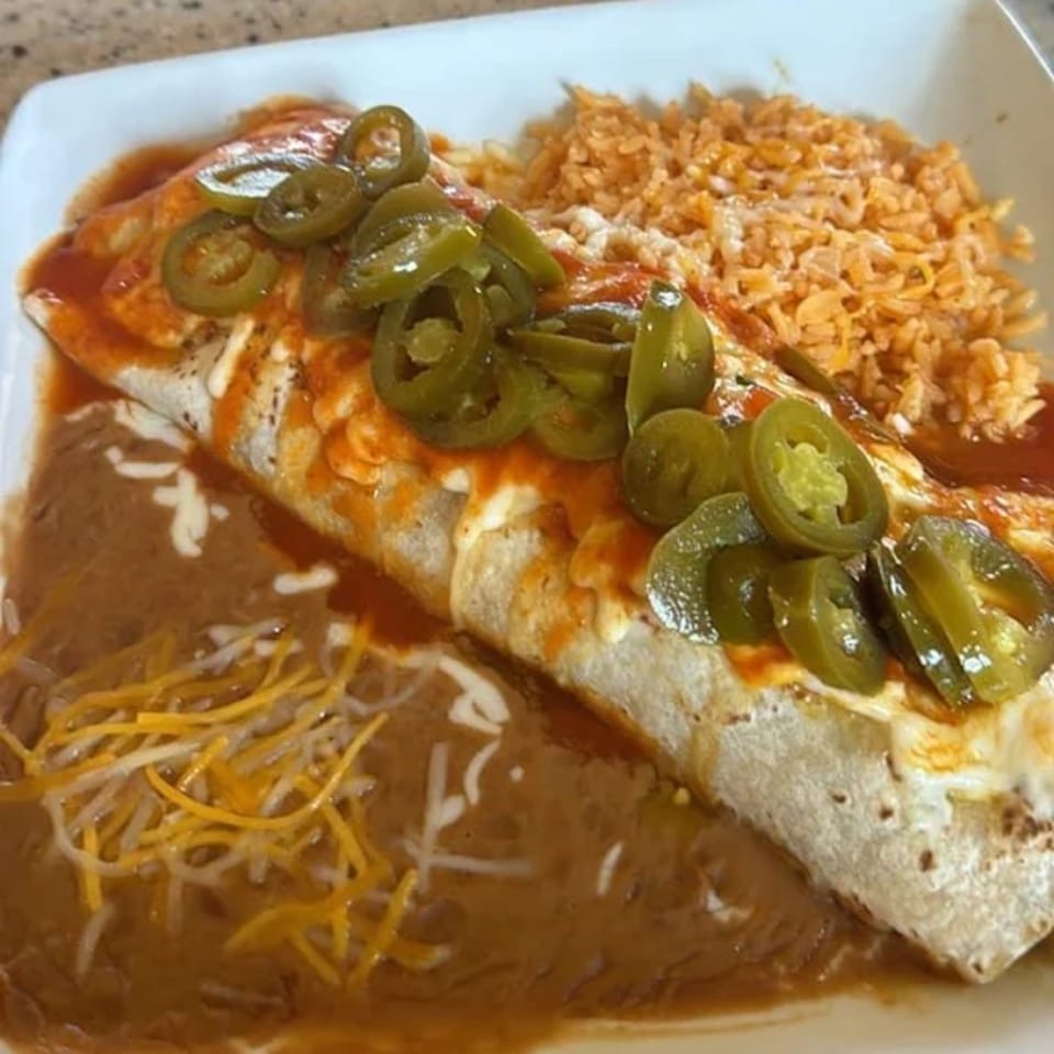 A La Esperanza burrito with red sauce, jalapeños, refried beans, and rice on a white plate.