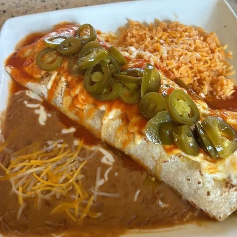 A La Esperanza burrito with red sauce, jalapeños, refried beans, and rice on a white plate.