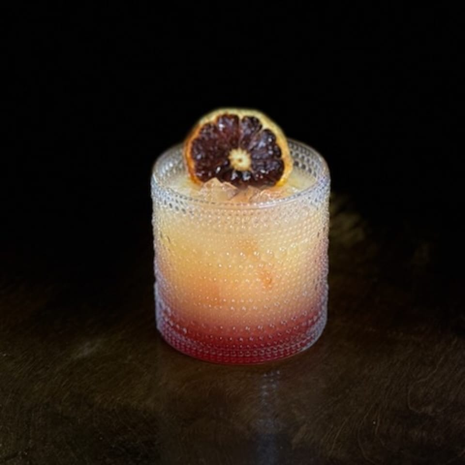 A La Esperanza Mexican cocktail with an orange-red gradient, garnished with a dried orange slice.