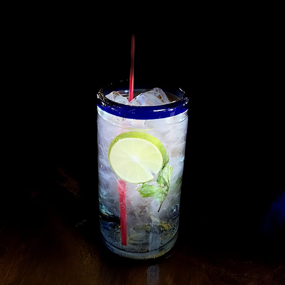 Refreshing La Esperanza mojito with lime, mint, and a red straw in a blue-rimmed glass.