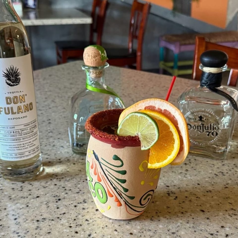 A La Esperanza Mexican restaurant drink in a decorated clay cup with citrus slices and tequila bottles.