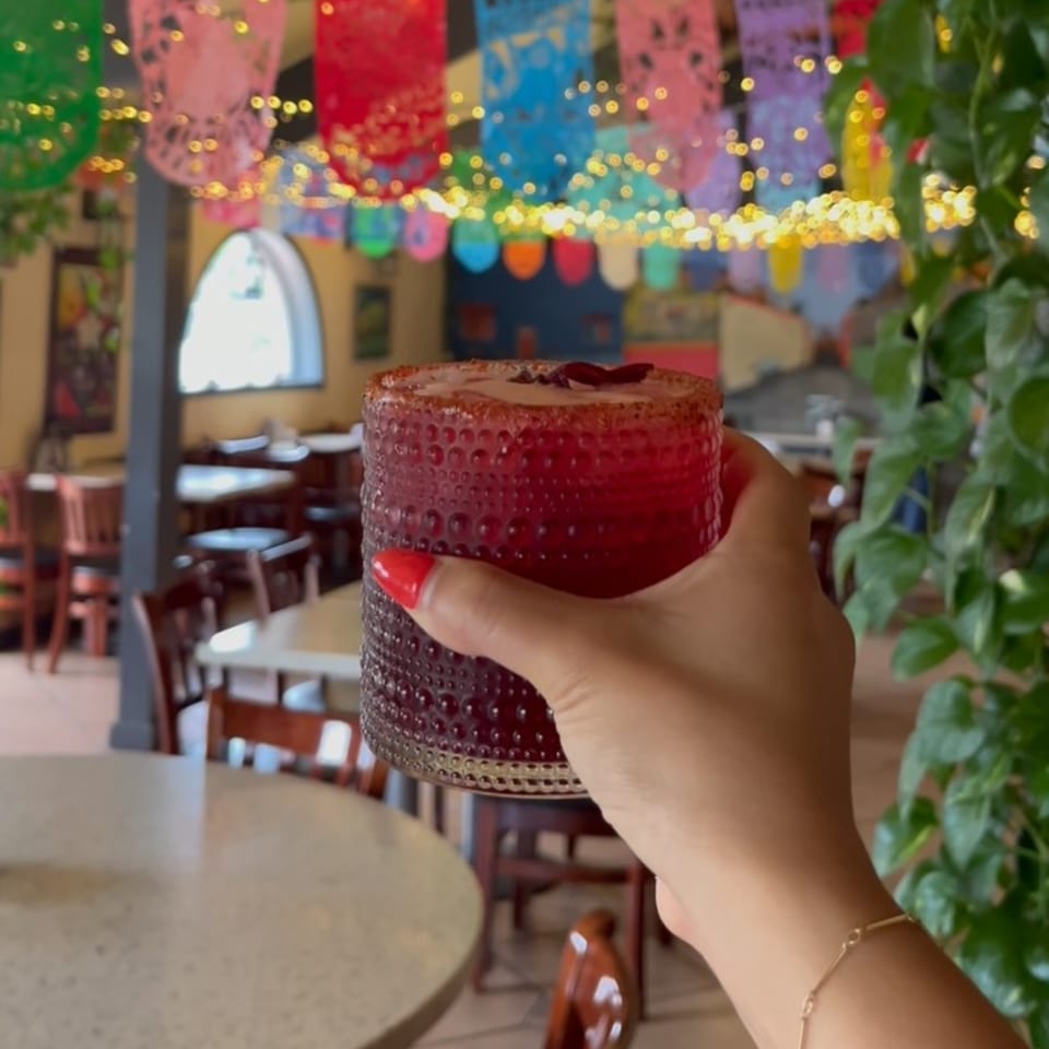 Hand holding a red drink with a chili-lime rim inside La Esperanza Mexican restaurant.