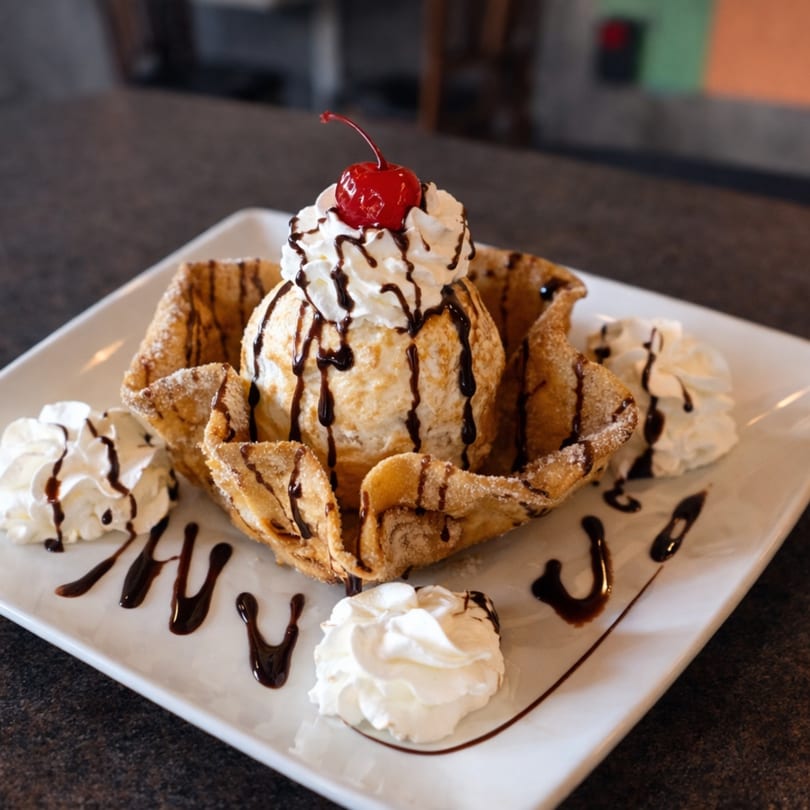 Fried ice cream in a crispy shell with whipped cream, chocolate drizzle, and a cherry.
